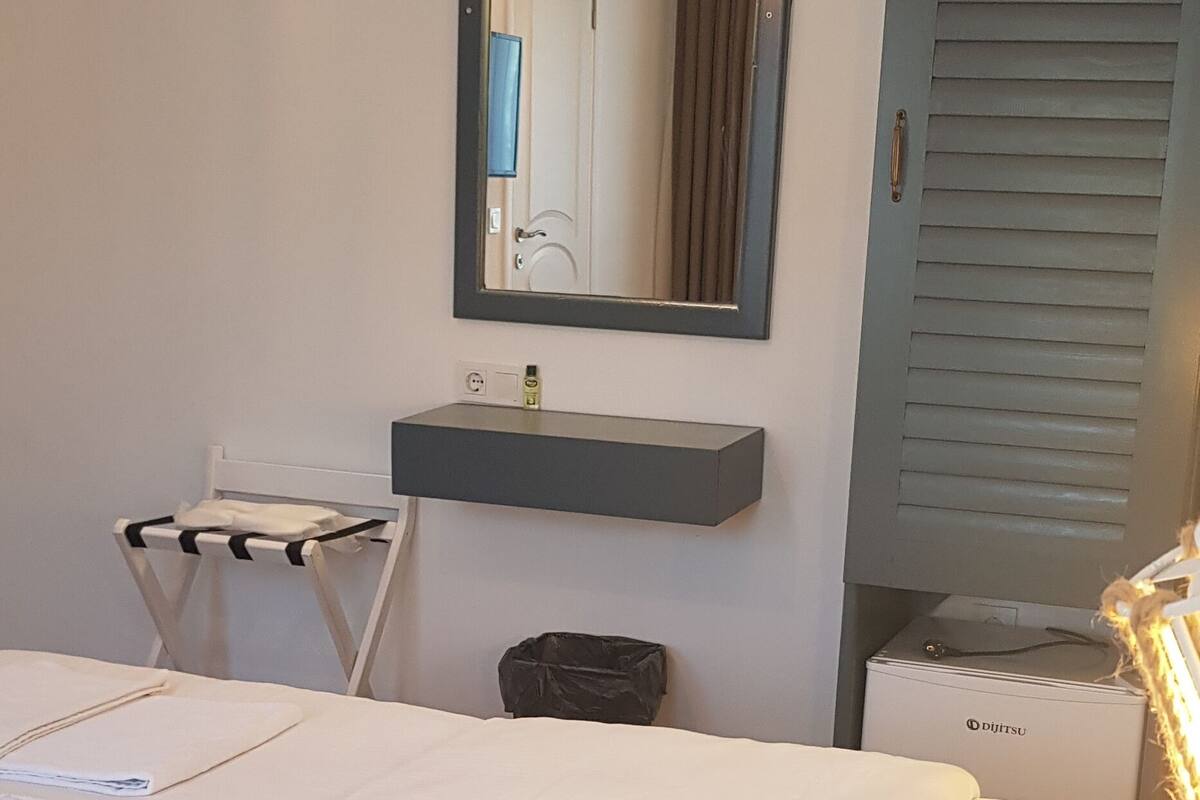 A hotel room with a bed, a small bedside table, a mirror, a shelf, and a wardrobe.