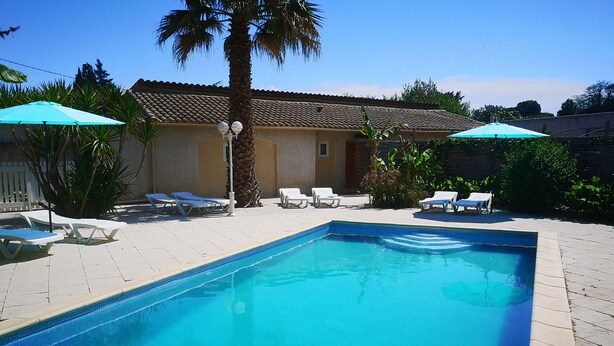 A rectangular swimming pool with clear blue water, surrounded by white lounge chairs and two green umbrellas.