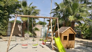 A playground with swings, a slide, and a wooden playhouse.