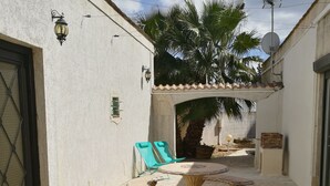 A courtyard with a stone floor, a round table with four chairs, a green chair, and a palm tree.