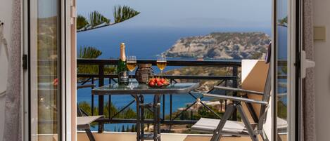 A balcony with a table set for two, featuring a bottle of wine, glasses, and a bowl of strawberries.
