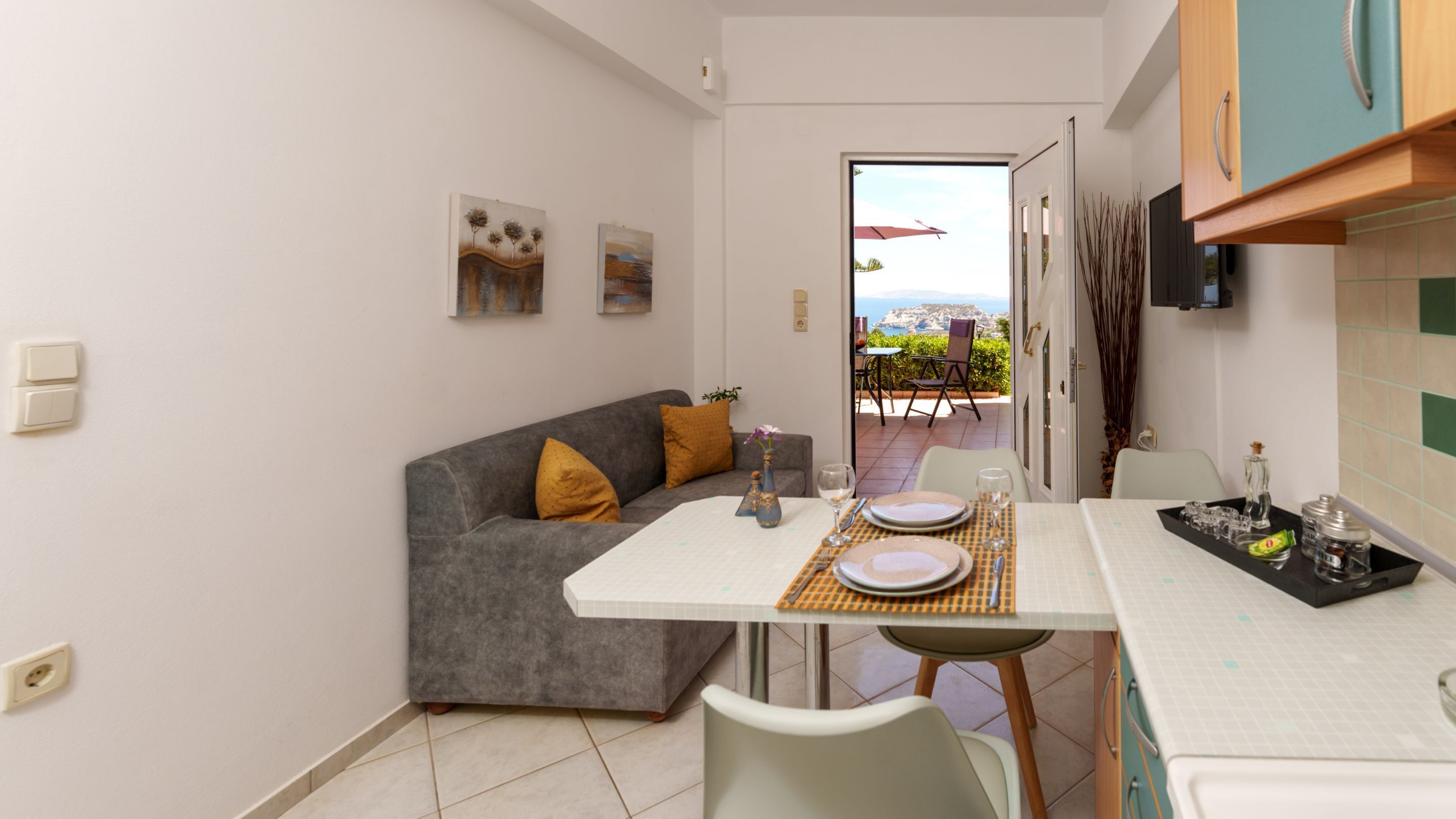 A compact living space with a kitchenette, a dining area, and a sofa. There is a view of the outdoors through a door.