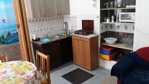 A compact kitchen with a sink, stove, and microwave. There is a dining area with a table and chairs. - Private House near Port of Piraeus (Piraeus)