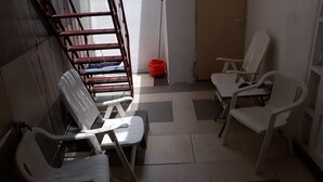A room with white plastic chairs, a metal rack with folded chairs, and a tiled floor. - Private House near Port of Piraeus (Piraeus)