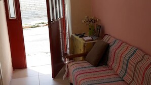 A room with a sofa, a small table with a vase and picture frame, and a door leading outside. - Private House near Port of Piraeus (Piraeus)