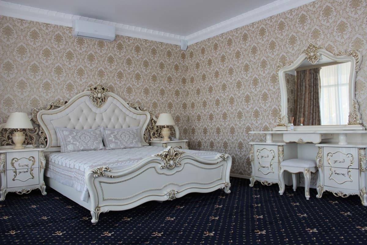 A classic, ornate bedroom with a tufted bed, a vanity with a mirror, and a patterned wallpaper.