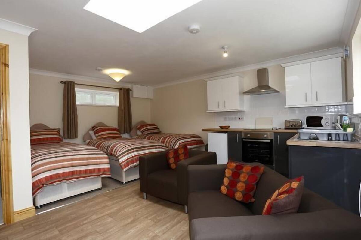 A compact room with two beds, a sofa, a kitchenette, and a window with curtains.