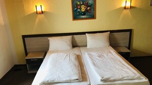 A double bed with two pillows and a folded blanket, a nightstand, and a wall-mounted painting. - Hotel restaurant germania (Bernkastel-Kues)