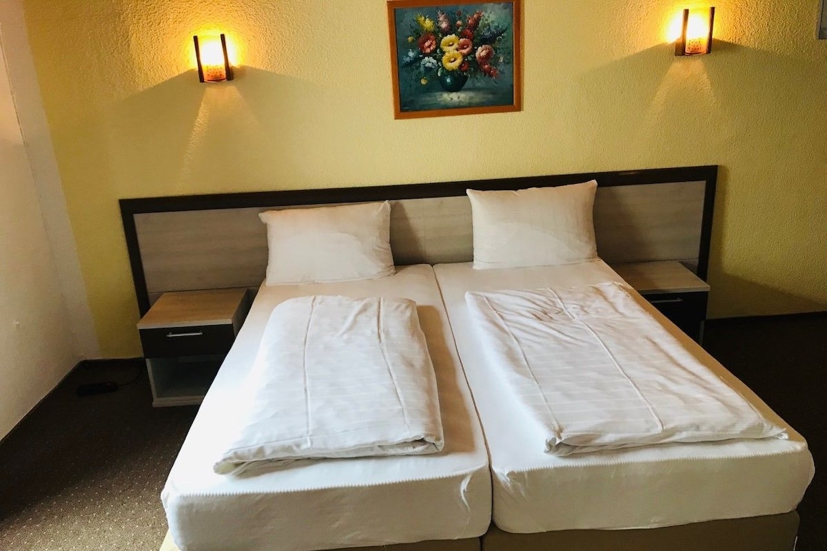 A double bed with two pillows and a folded blanket, a nightstand, and a wall-mounted painting.