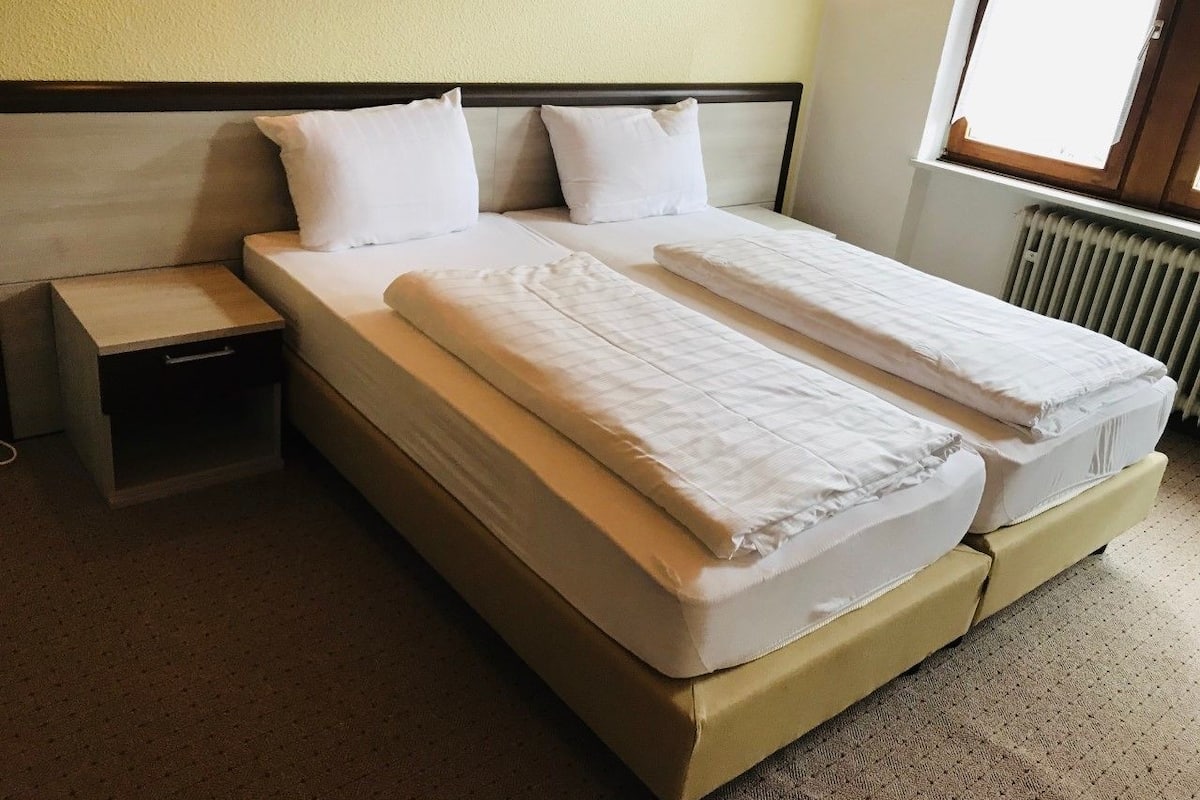 A double bed with two pillows, a nightstand, and a window with a view.