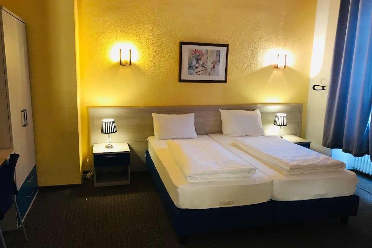 A hotel room with a double bed, two bedside tables with lamps, a small desk, and a chair.