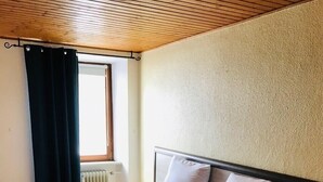 A neatly made bed with two pillows, a bedside table, and a window with curtains. - Hotel restaurant germania (Bernkastel-Kues)