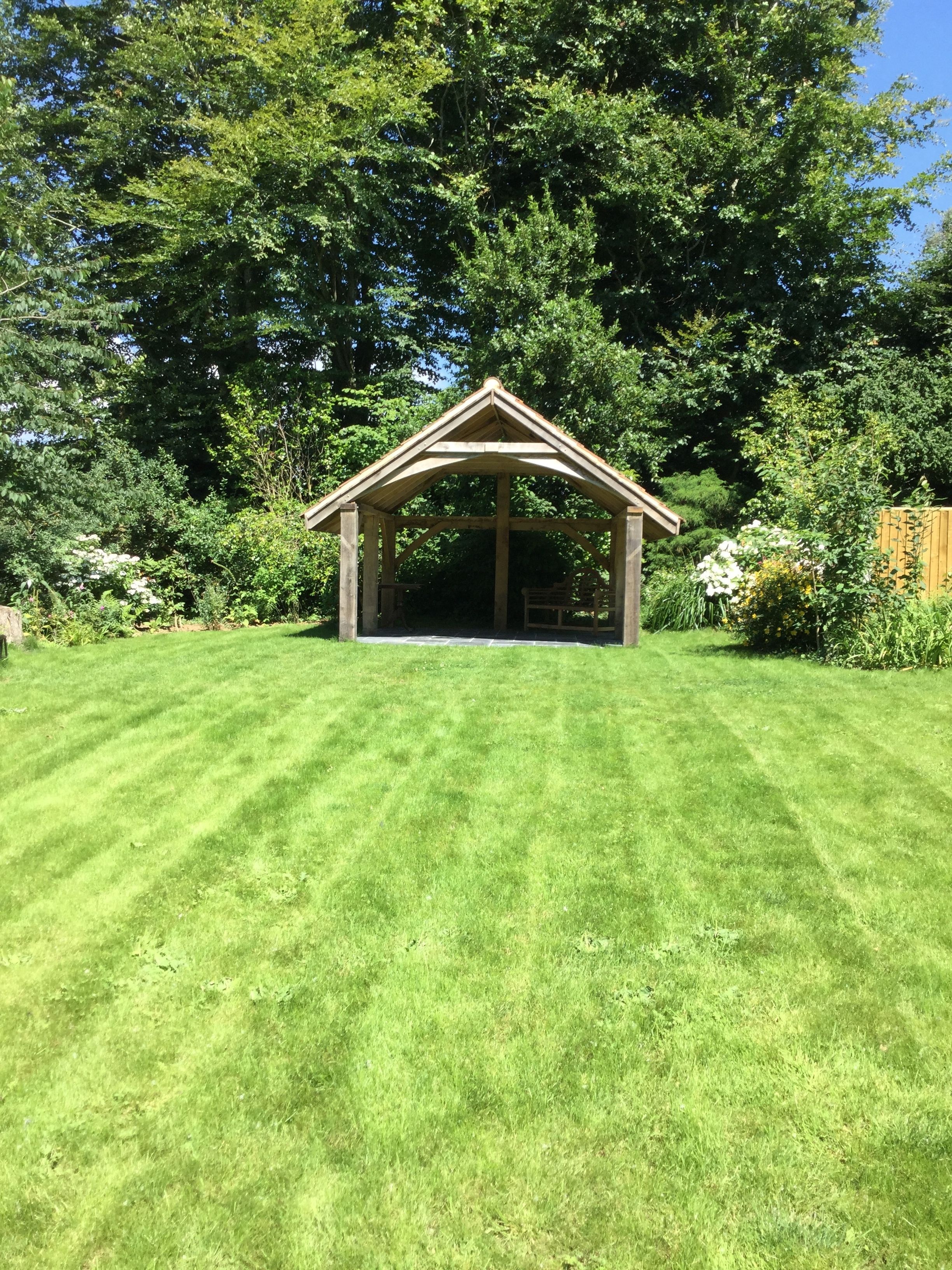 A gazebo with a triangular roof in a well-maintained grassy area surrounded by dense trees.