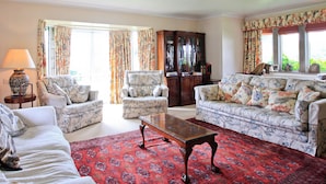 A living room with floral-patterned sofas, a wooden coffee table, and a red patterned rug. - Oxbridge Farm (Bridport)