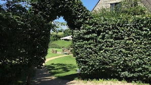 A gravel path leading to a stone building with a triangular roof, surrounded by dense green hedges. - Oxbridge Farm (Bridport)
