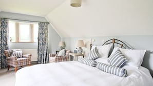 A bedroom with a large bed, two chairs, a nightstand, and a window with curtains. - Oxbridge Farm (Bridport)