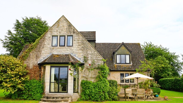 A stone house with a triangular roof, a front porch, and a patio with outdoor furniture. - Oxbridge Farm (Bridport)