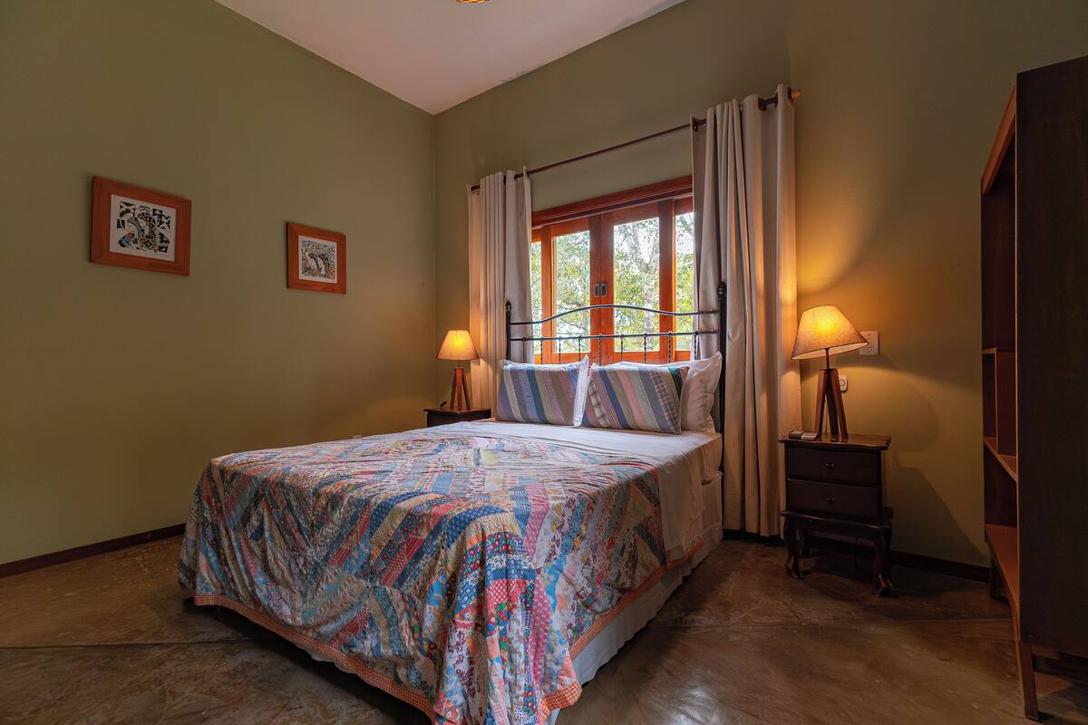 Une chambre à coucher avec un lit, deux lampes de chevet, une fenêtre avec des rideaux et deux tableaux encadrés accrochés au mur.