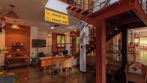 Un espacio habitable amplio con una escalera de madera, un letrero de registro de entrada/salida y un comedor con sillas de mimbre.