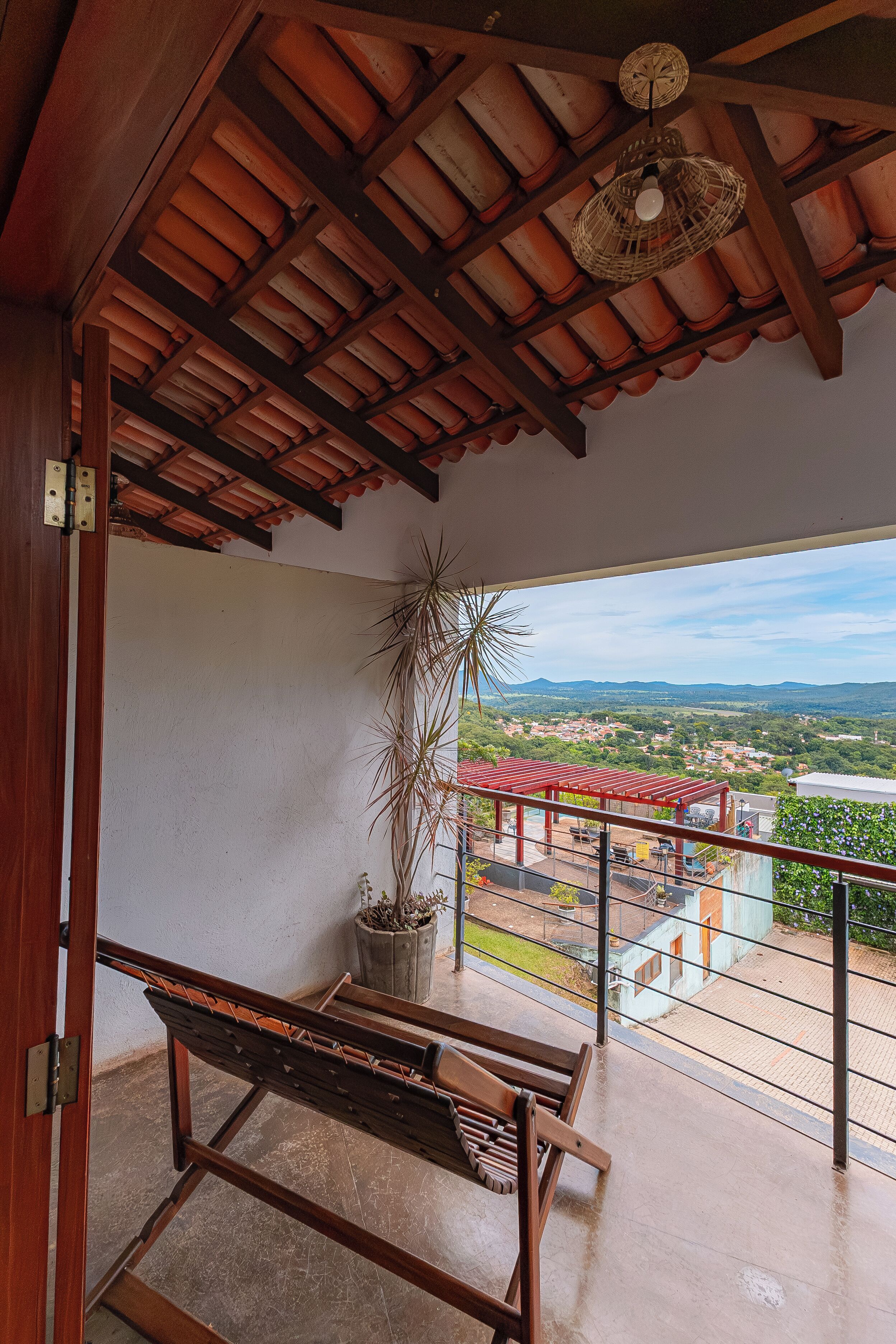 Un balcón con un banco de madera, una planta en maceta y vistas a un pueblo y montañas.