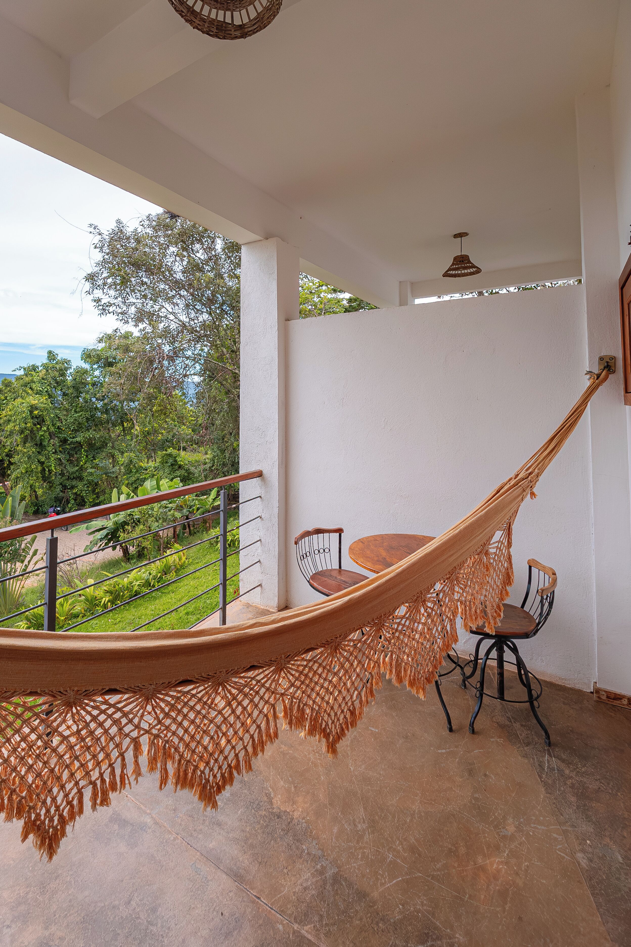Una silla hamaca en un balcón con vistas a zonas verdes y una mesa con sillas.