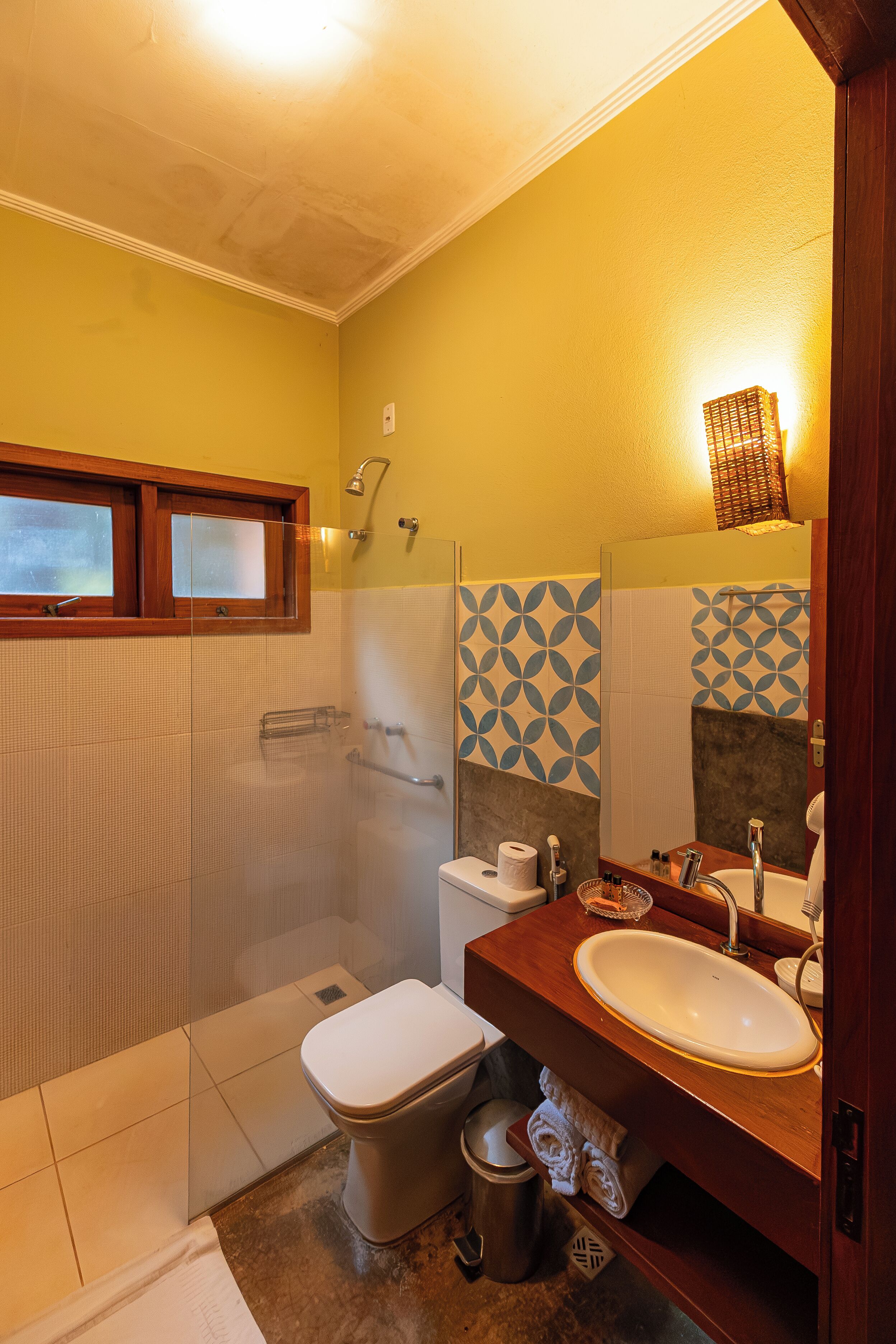 A bathroom with a toilet, sink, shower, and a window.