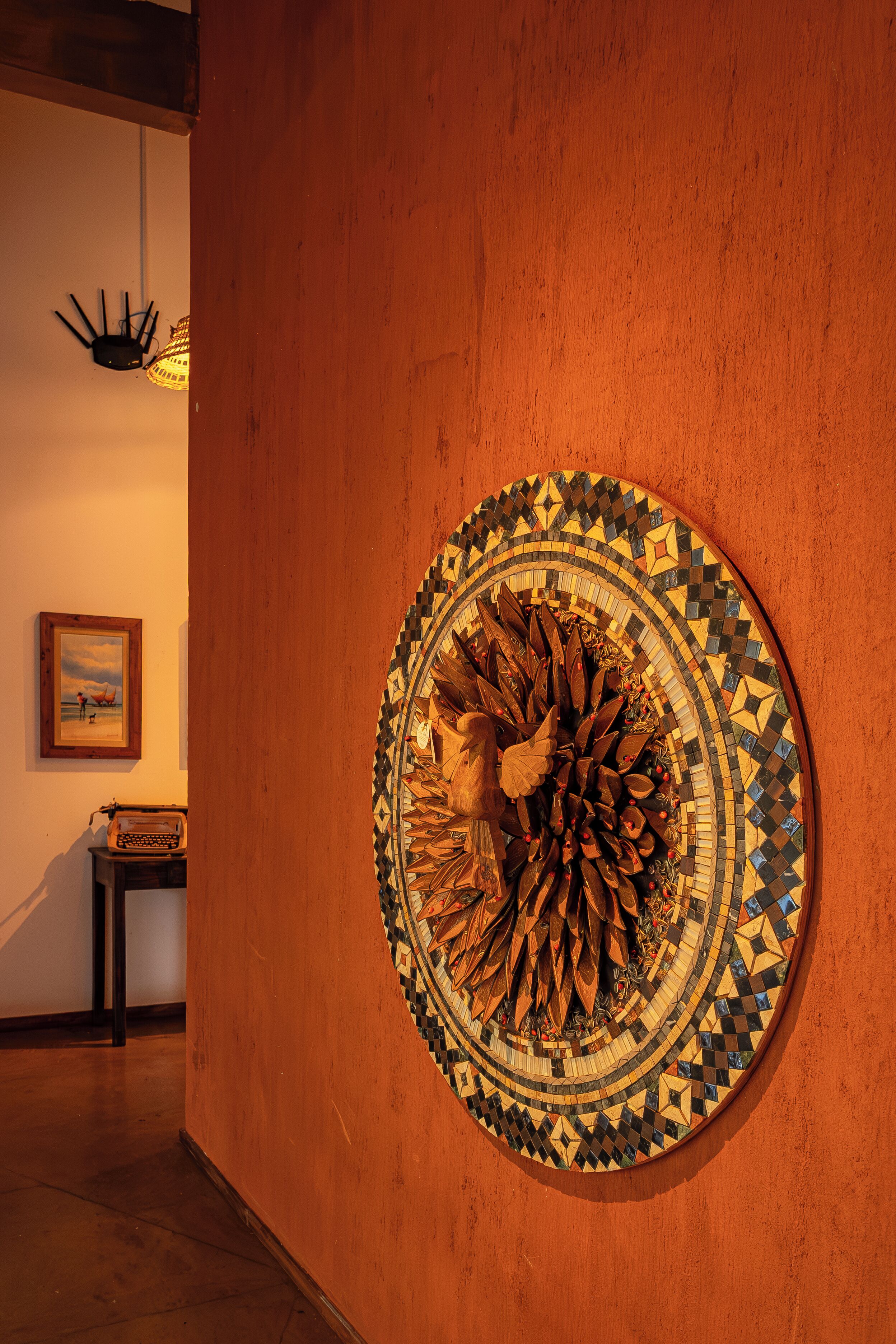 Uma obra de arte em mosaico circular na parede, um quadro emoldurado na parede vizinha e uma máquina de escrever antiga sobre uma mesa pequena.