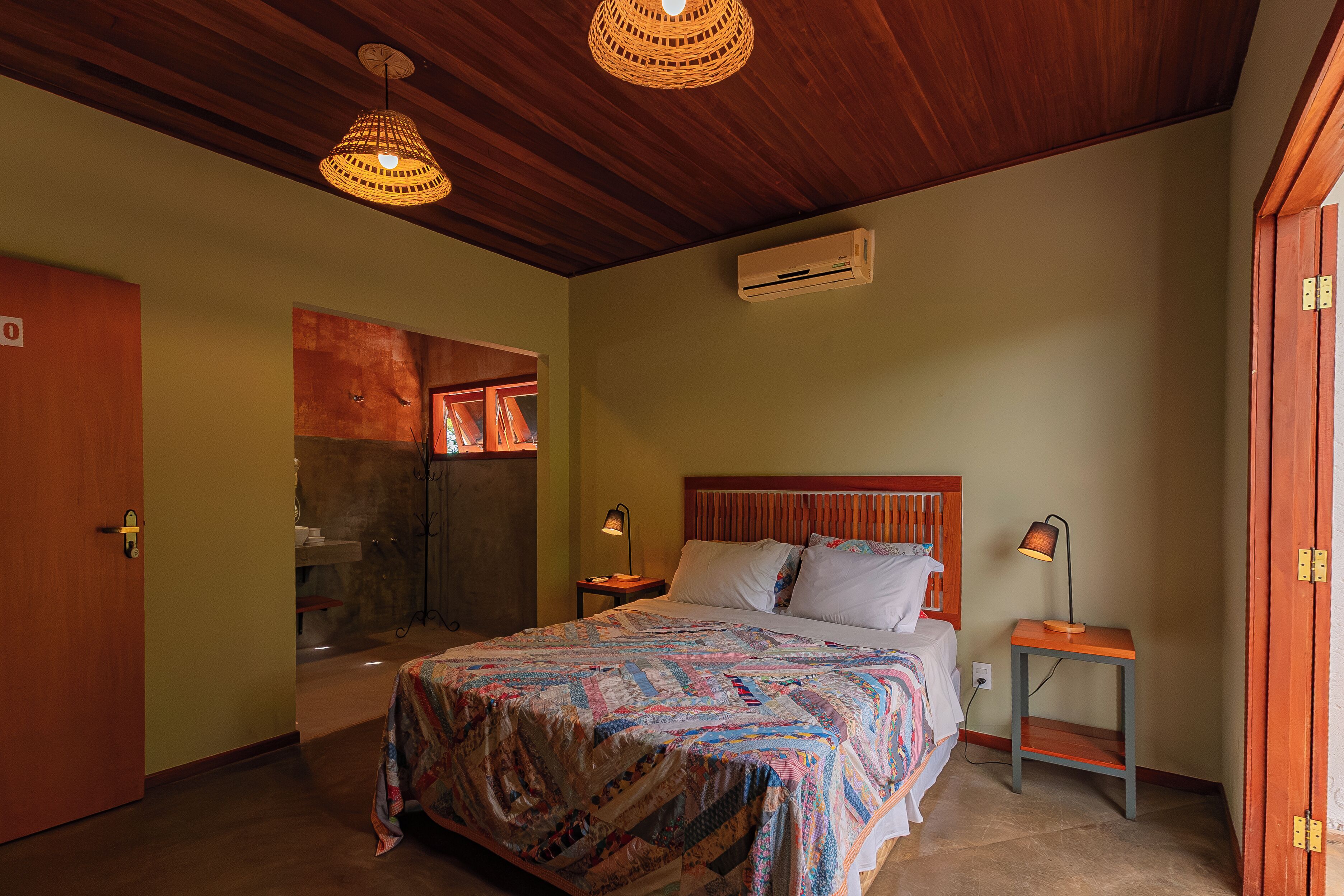 Quarto com cama, duas mesas de cabeceira, ar condicionado fixado na parede e teto de madeira.