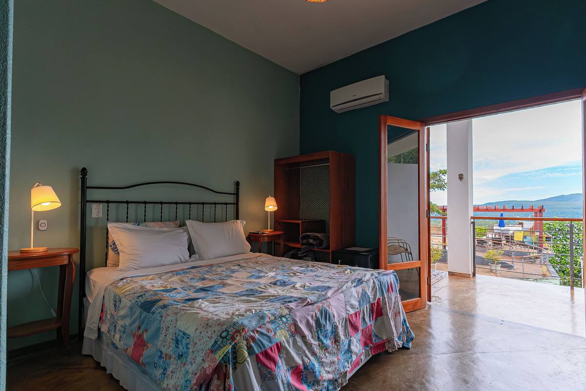 Une chambre à coucher avec un lit, des lampes de chevet, une armoire en bois et un balcon avec vue.