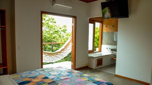 Un dormitorio con cama, una hamaca, un baño con lavamanos y un televisor montado en la pared.