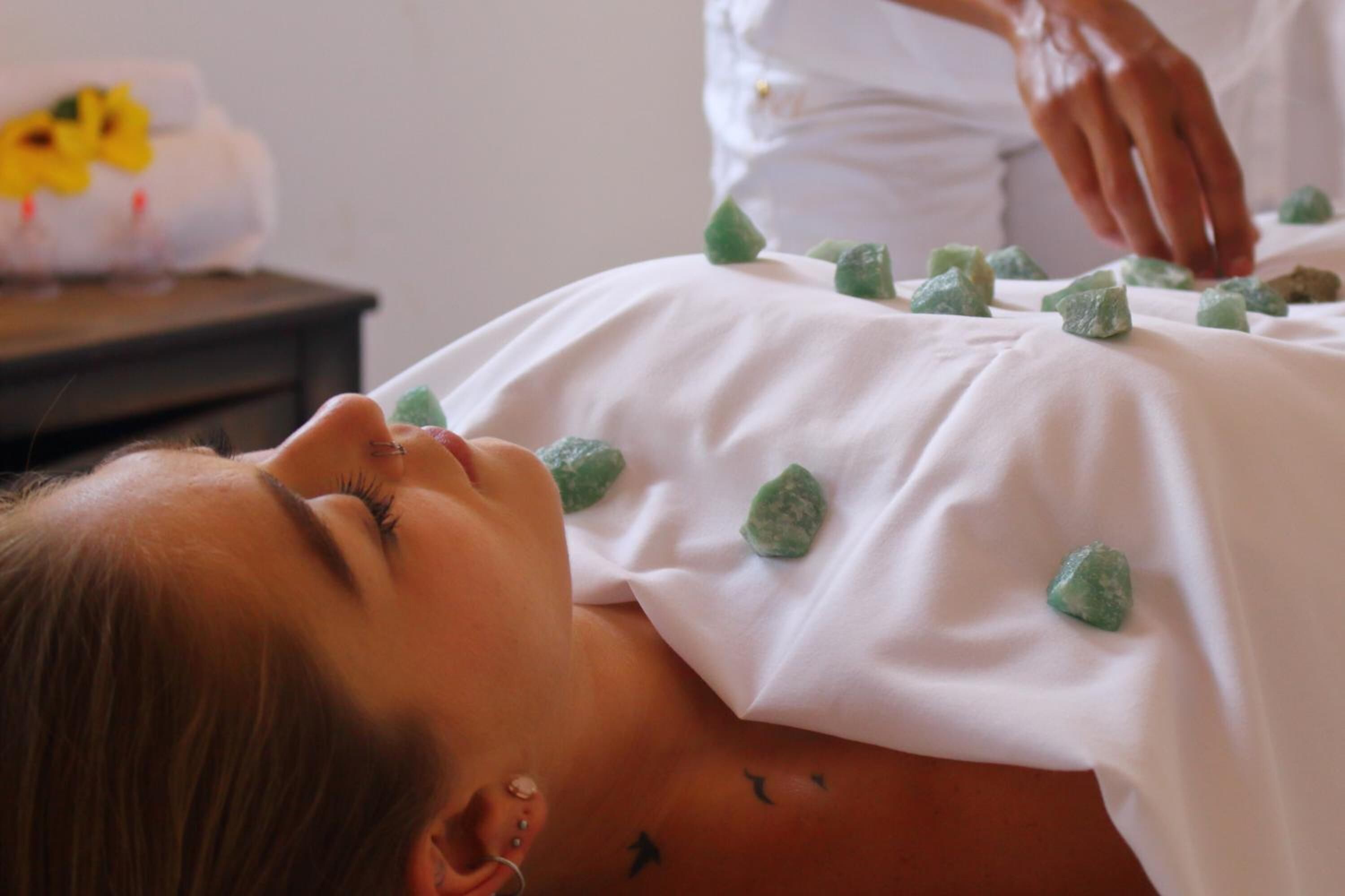 A person lying down with green stones placed on their back.