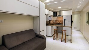 Un espacio habitable compacto con sofá, kitchenette y una pequeña zona de bar.