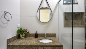 Un baño con encimera de granito, un lavabo blanco, un espejo redondo, un tozaleta, una planta en maceta y un dispensador de jabón.