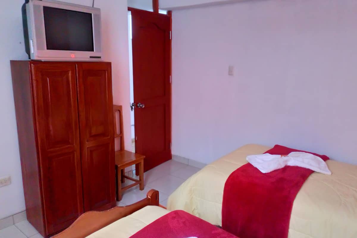 A room with two beds, a wooden wardrobe, a television on top, and a red door.