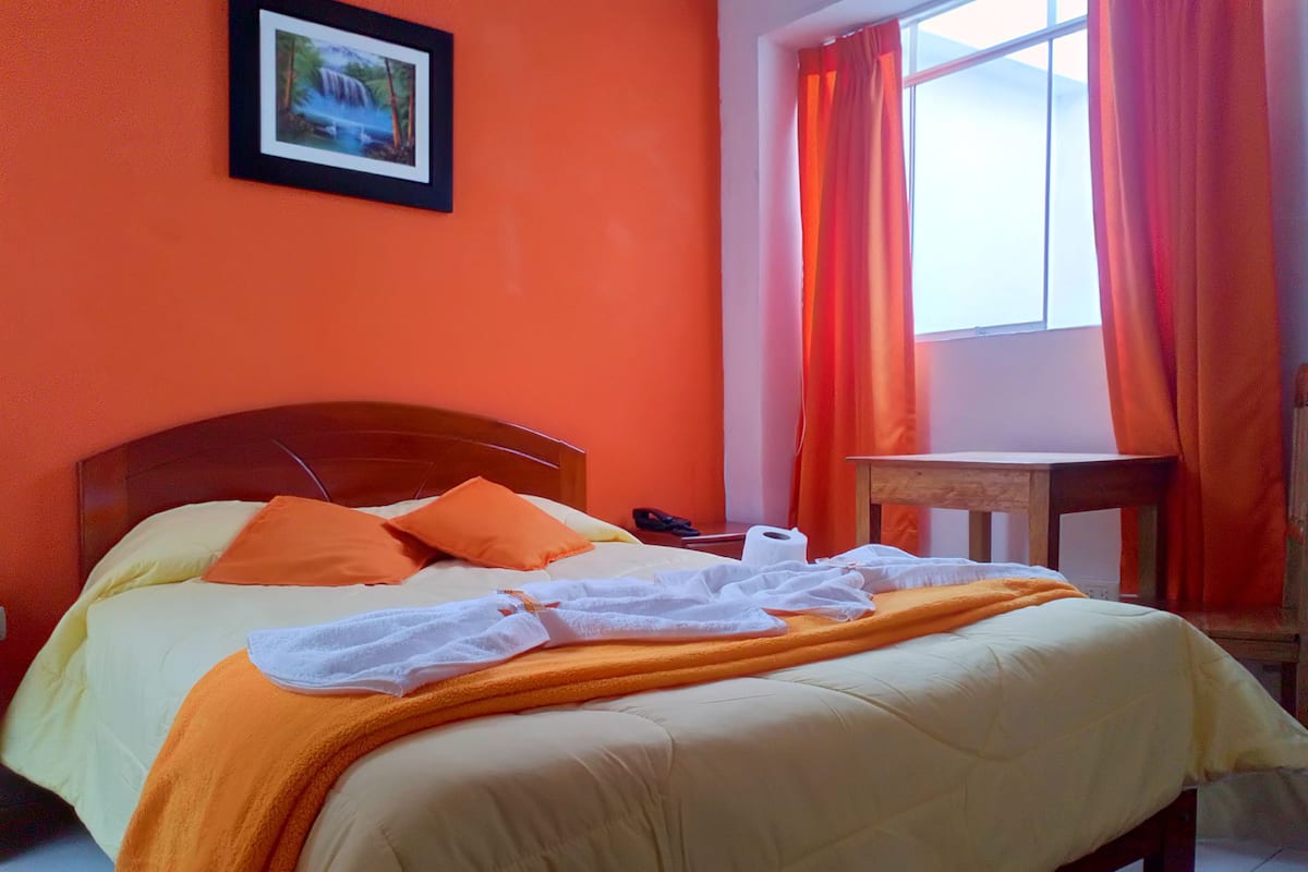 A bed with orange and white bedding, a wooden headboard, and a framed picture on the wall.