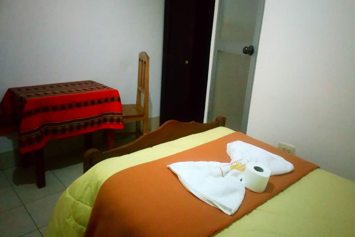A hotel room with a bed, a table with a red tablecloth, a chair, and a wardrobe.
