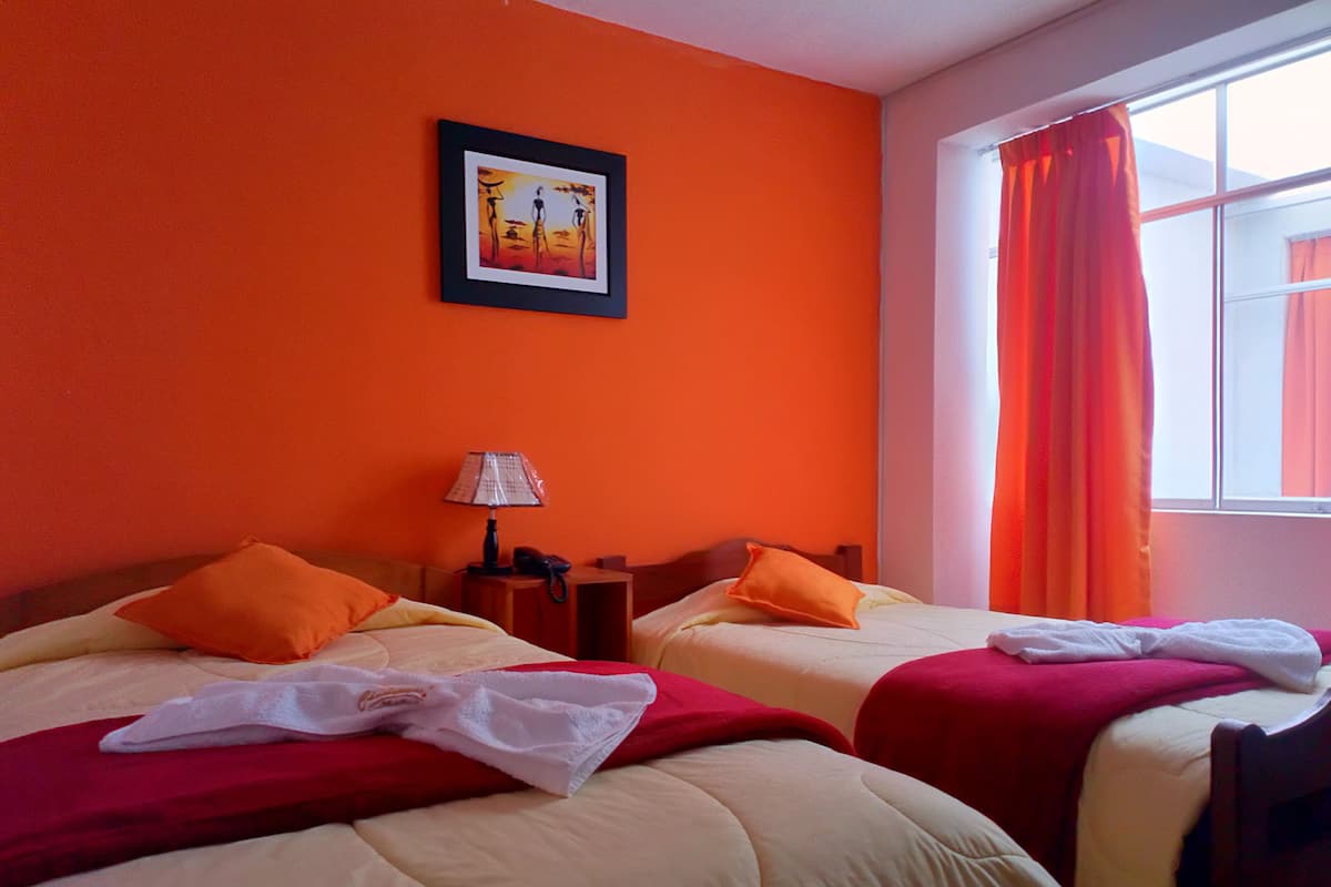 A hotel room with two beds, orange walls, a framed picture on the wall, a lamp, and a window with curtains.