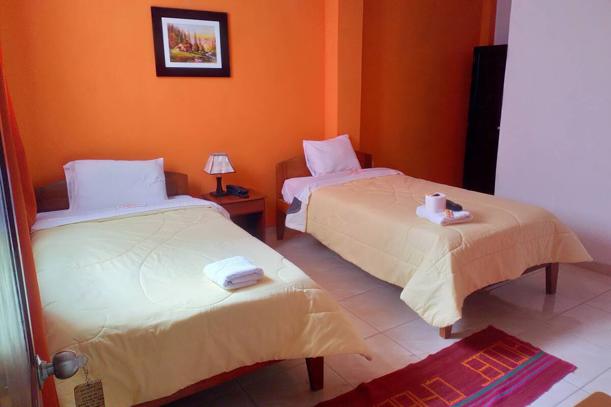 A hotel room with two beds, a nightstand, a lamp, and a framed picture on the wall.