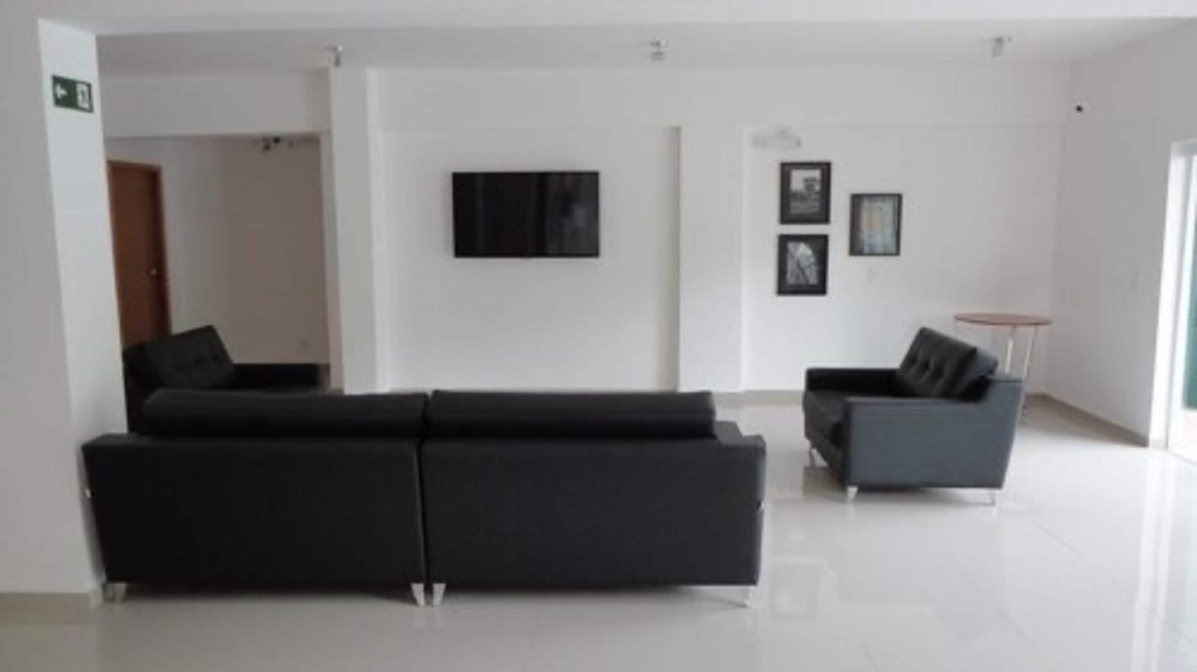 A modern living room with a black sofa, a grey armchair, a flat-screen TV mounted on the wall, and two framed pictures.