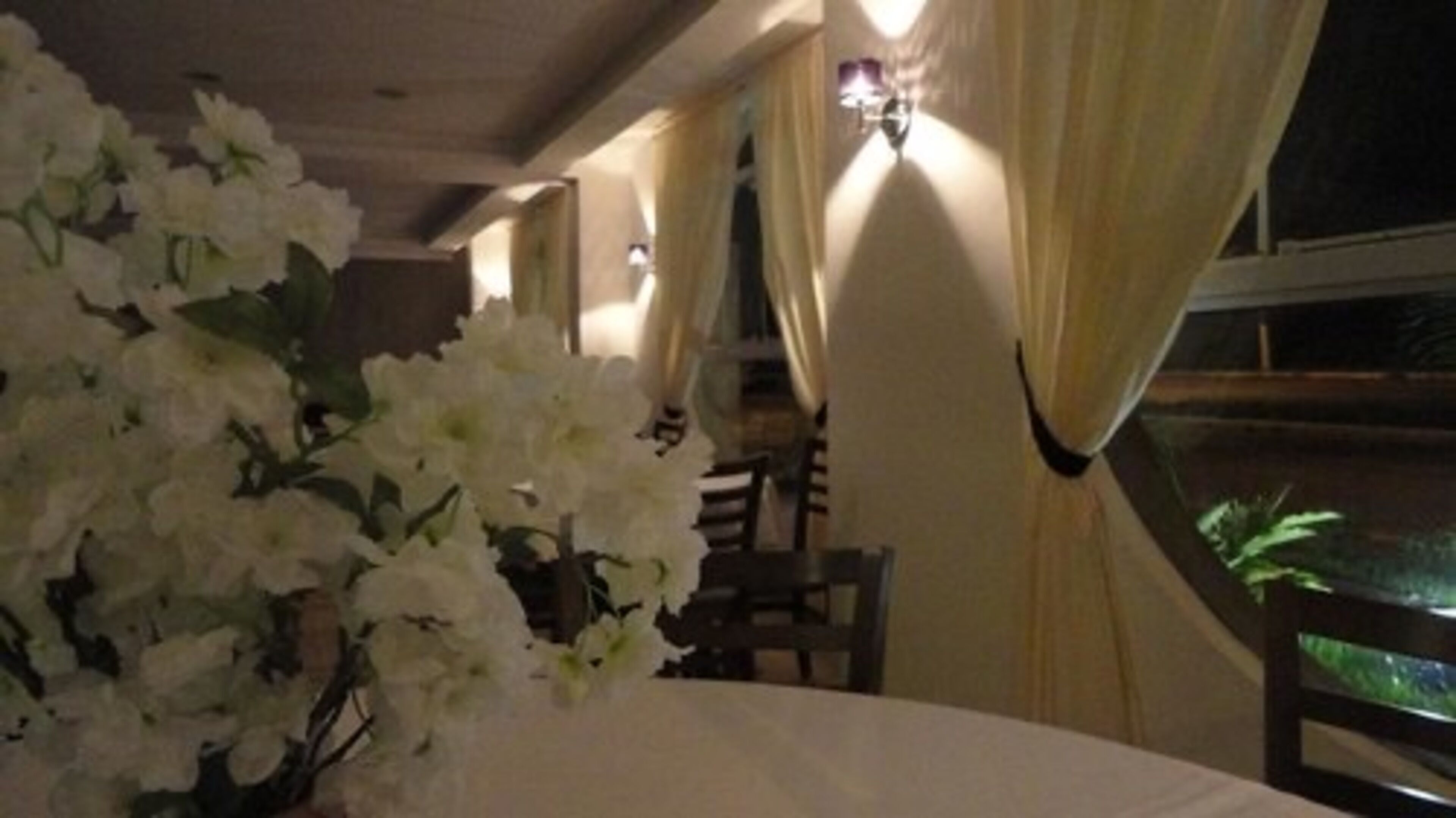 A dining area with a table set for two, featuring a vase of white flowers.