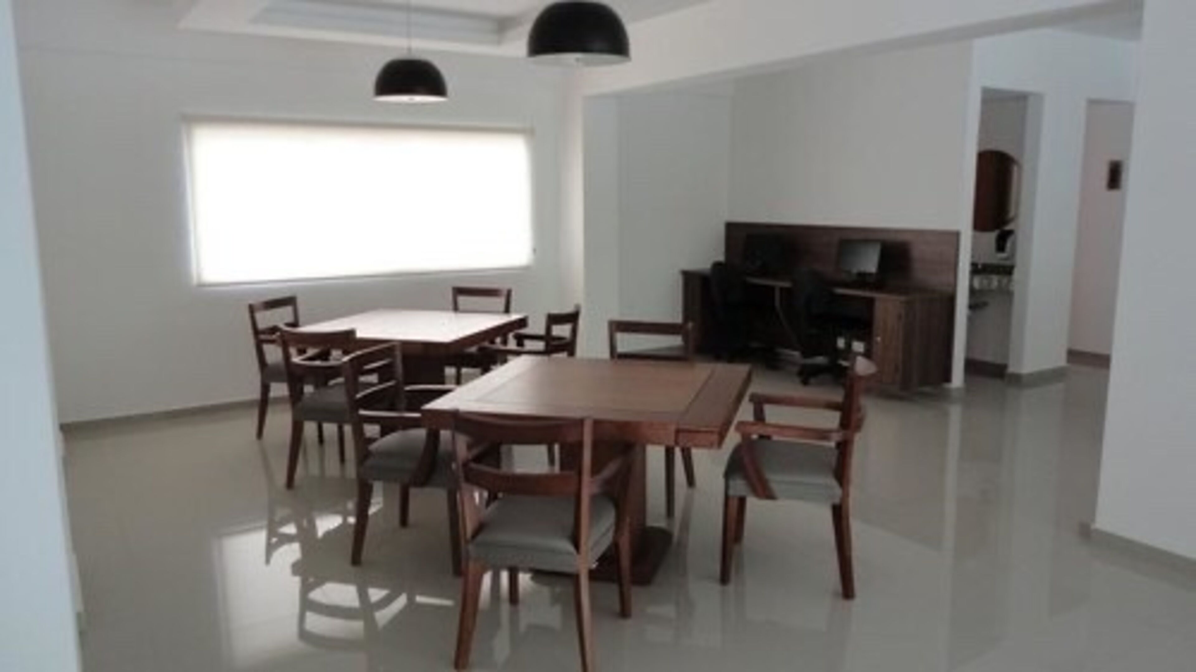 A spacious room with a large dining table surrounded by chairs, a television, and a kitchenette.