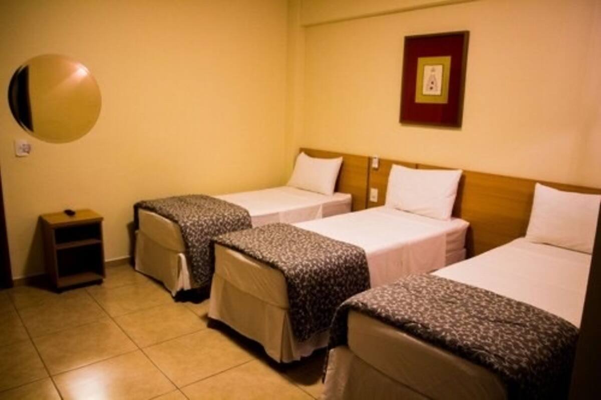 Une chambre d’hôtel avec trois lits simples, une petite table de chevet et un miroir rond fixé au mur.