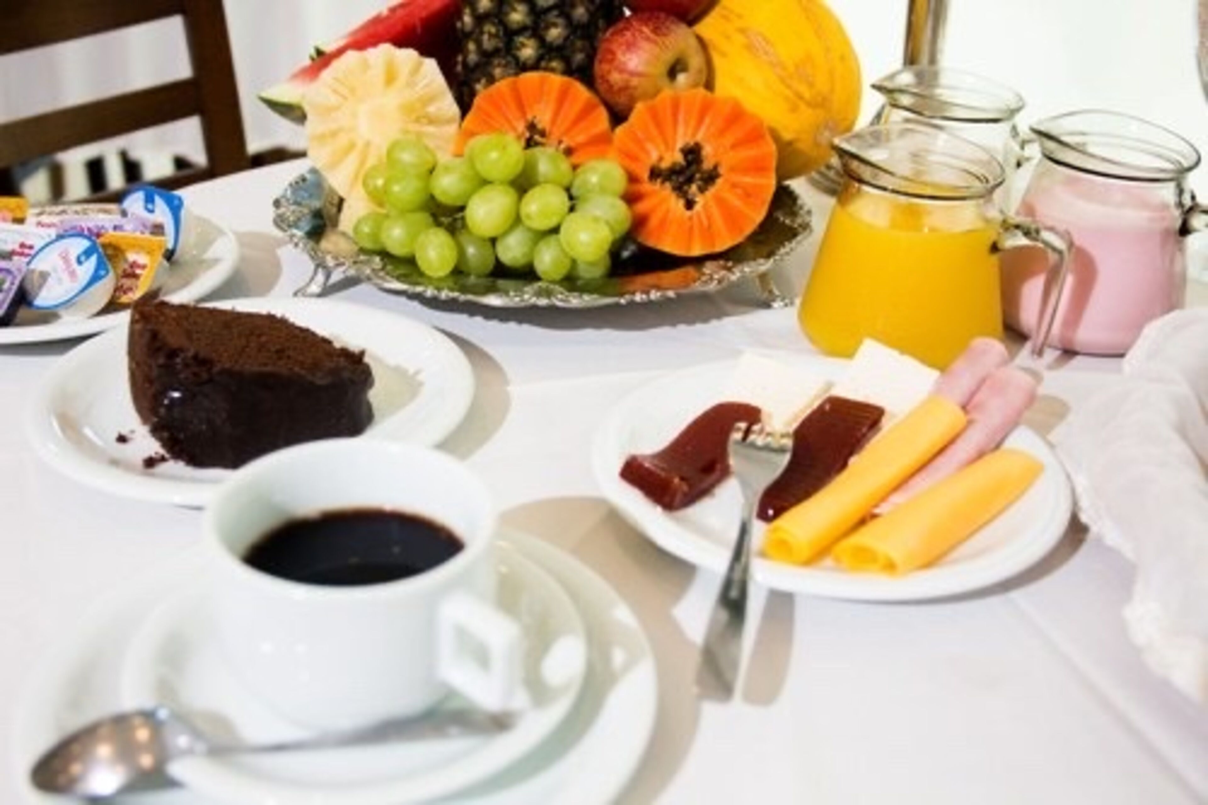 A breakfast table with various food items including a slice of cake, fruits, and beverages.