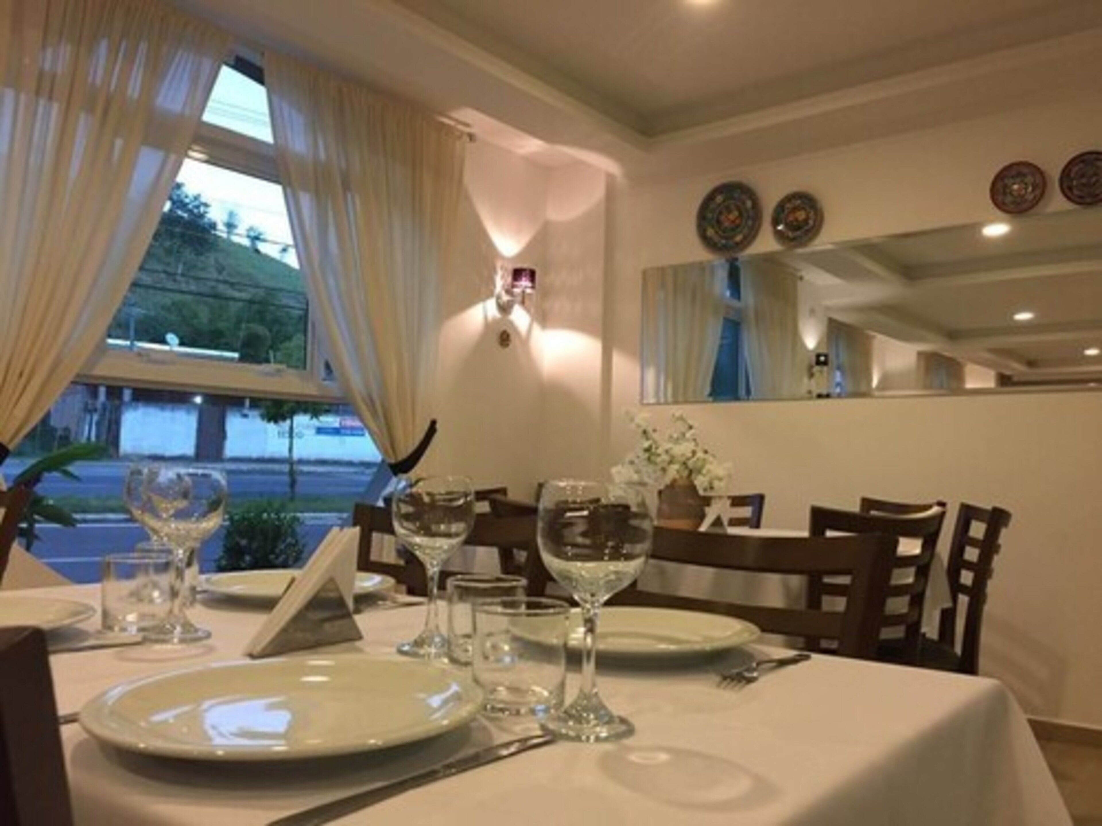 Une table à manger dressée avec des assiettes, des verres et des couverts, donnant sur l’extérieur par une fenêtre.