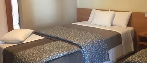 A hotel room with two beds, a nightstand, a framed picture on the wall, and a door leading to another room.