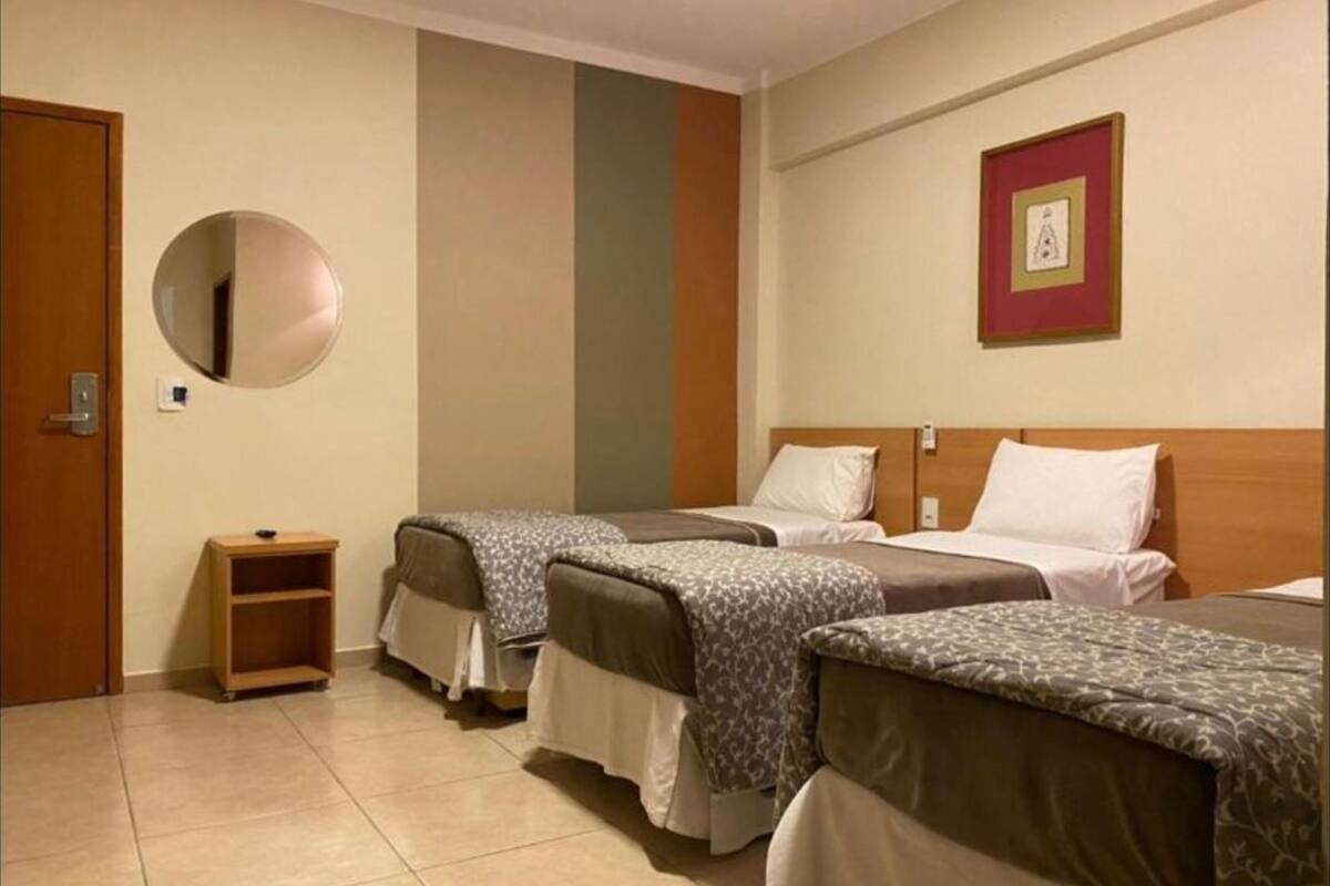 Une chambre d’hôtel avec deux lits simples, une petite table de chevet en bois, un miroir rond et un tableau encadré au mur.