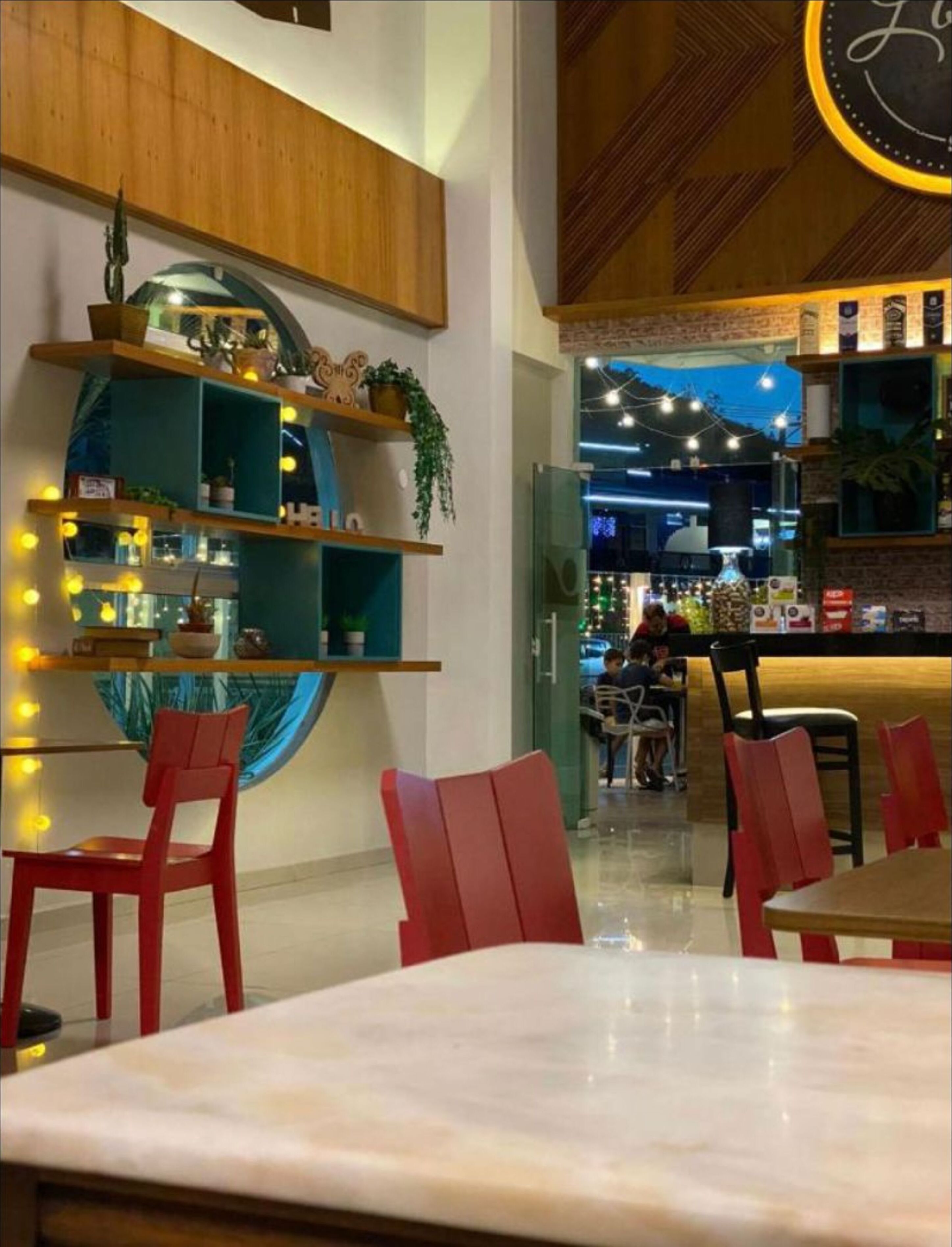 A restaurant interior with wooden shelves, red chairs, and a bar area.