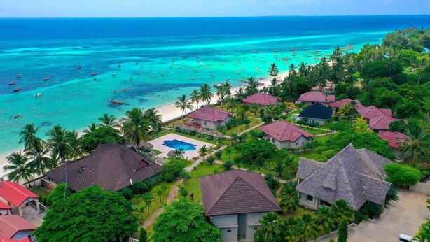 Een tropisch resort met meerdere bungalows, een zwembad en een strand met boten.