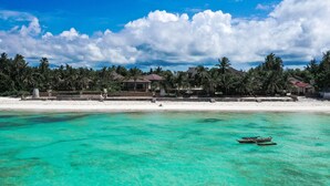 Een strandresort met helder turquoise water, palmbomen en een rij huizen met rode daken.