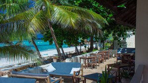 Een terras aan het strand met lounge stoelen en tafels, met uitzicht op de oceaan.